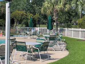 Zona de piscina con sillas reclinables verdes y sombrillas, piscina cercada y cartel que indica cierre de la piscina.