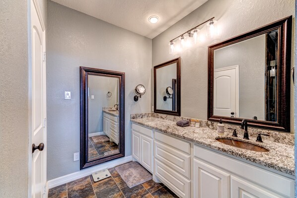A bathroom with a double sink vanity, a large mirror, and a light fixture above the mirror. - Modern Farmhouse w/ Hill Country Views, EV, Wineries, Large Patio (Dripping Springs)