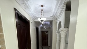 Un couloir orné d’un lustre, avec une porte en bois et une colonne blanche.