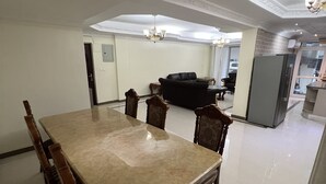 Un grand espace dédié à la salle à manger, avec une grande table rectangulaire et quatre chaises, un canapé noir et un réfrigérateur en arrière-plan.
