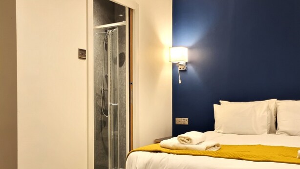 Habitación de hotel con cama, ducha y lámpara fijada a la pared.