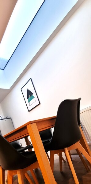 A dining area with a wooden table and black chairs, a framed geometric artwork on the wall, and a view of the sky through a skylight. - Modern 6 Bedroom 4 Bath House w Parking (Swindon)