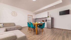 A modern living room with a sofa, a dining table with chairs, and a kitchen area with cabinets and a refrigerator. - Holiday home with terrace near the sea (Šilo)