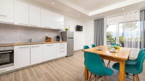 A modern kitchen with white cabinets, a stainless steel refrigerator, and a wooden dining table with teal chairs. - Holiday home with terrace near the sea (Šilo)