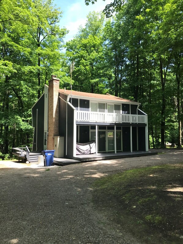 A two-story cabin with a balcony, surrounded by trees.