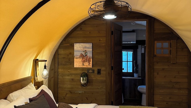 A cozy, arched bedroom with a bed, pillows, a quilt, a wall-mounted light, and a painting. - Hansen Inn and Cabins (Wall)