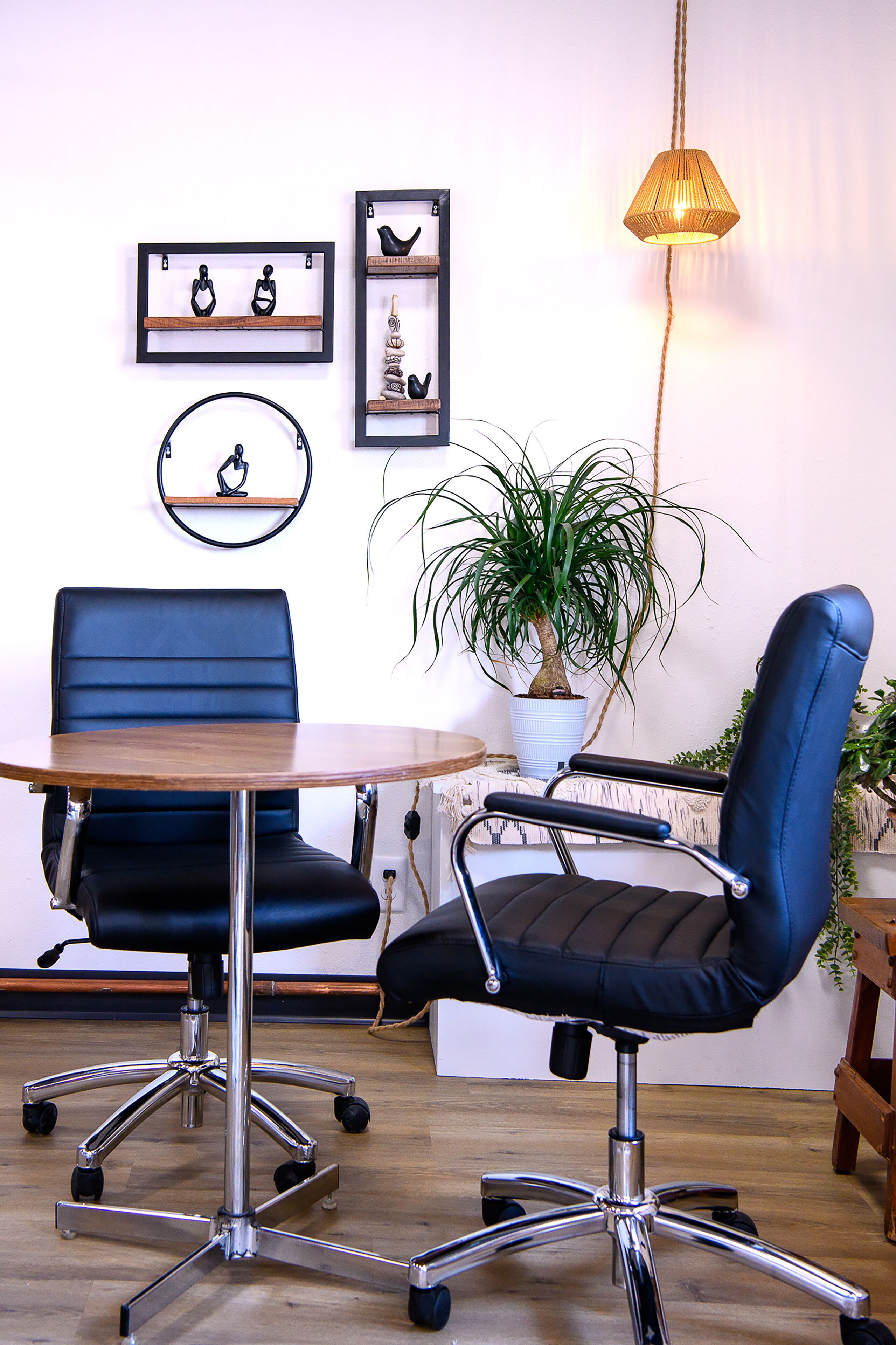 Una habitación con dos sillas de oficina azules, una mesa de madera, una lámpara colgante y estanterías con adornos.