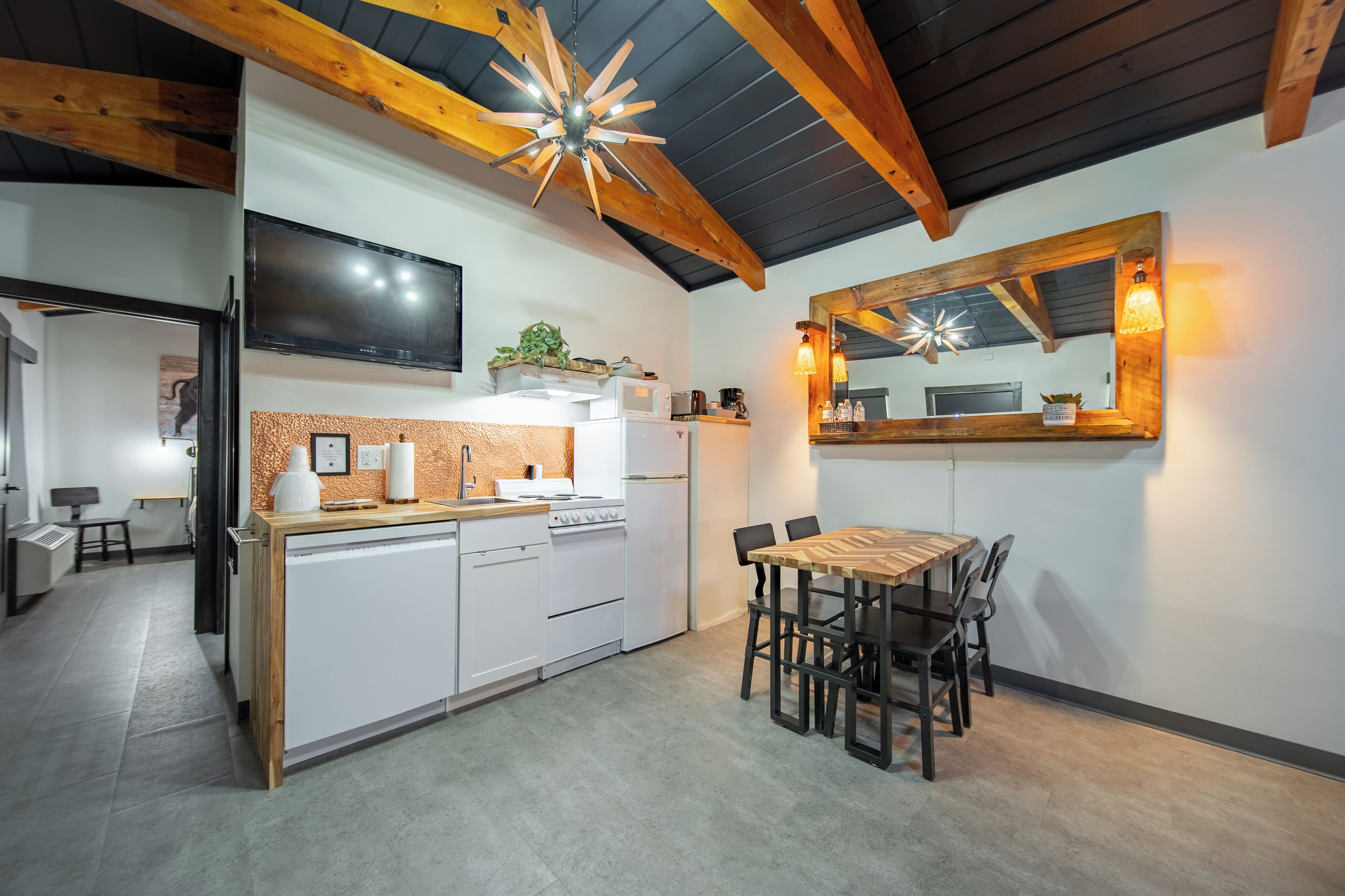 A modern kitchen with white cabinets, a wooden dining table, and a ceiling fan.
