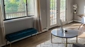 A spacious room with large windows, a round table, a bench, and a white rug. - Red Cabin Lake House with Amazing Views! (Vernon Township)