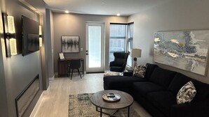 Un salon moderne avec un canapé noir, une table basse et un téléviseur fixé au mur.