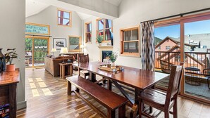 A spacious living area with a wooden dining table, benches, and a fireplace. Large windows offer views of the surrounding landscape. - The Baldwin - Luxury Penthouse in the Heart of Keystone - Ski In/Out• $0 Cleaning Fee (Keystone)