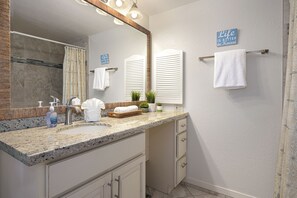 Une salle de bain dotée d’un comptoir en granit, de deux lavabos, d’un grand miroir et d’un porte-serviettes.