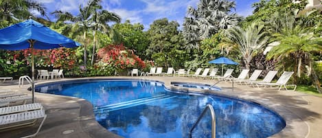 A swimming pool with lounge chairs and umbrellas, surrounded by tropical vegetation.