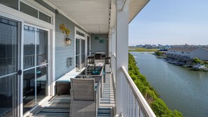 A balcony with wicker furniture, a glass door, and a view of a river with boats.