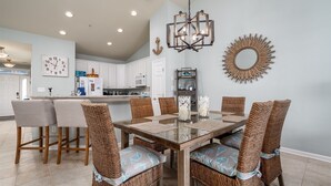 A dining area with a glass-top table, wicker chairs, and a chandelier.