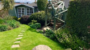 A garden with a pathway leading to a house with a green door and windows. - Mulberry Cottage Coastal Holiday Home (Cowes)