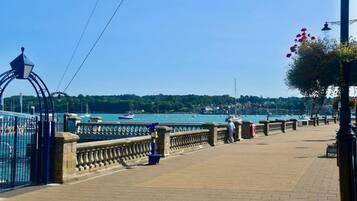 A waterfront promenade with a stone balustrade, a metal gate, and a row of street lamps.