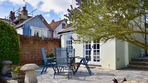 A patio with stone flooring, a table and chairs, and a tree with purple flowers. - Mulberry Cottage Coastal Holiday Home (Cowes)