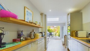 A narrow kitchen with wooden countertops, a coffee machine, and a toaster. There is a window providing natural light and a view of the outdoors. - Blackberry Cottage Bembridge Accessible Coastal Holiday Home (Bembridge)
