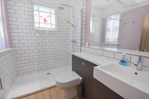 A modern bathroom with white tiled walls, a glass shower enclosure, a white toilet, and a sink with a mirror above it. - Arden Villa With Sea Views (Ryde)