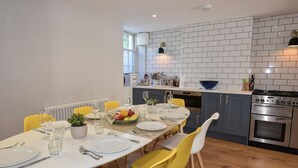 Een moderne keuken met een witte bakstenen achterwand, een eethoek met gele stoelen en een ingebouwde oven.