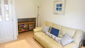 A living room with a beige sofa, a bookshelf, and a framed picture on the wall. - Solent Landing No 12A - Beachfront (Bembridge)