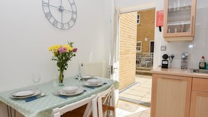 A dining area with a table set for four, a vase with flowers, and a clock on the wall. - Solent Landing No 12A - Beachfront (Bembridge)