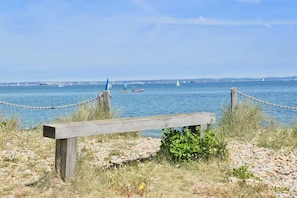 A wooden bench by a rocky shore with a view of the sea and distant cityscape. - Solent Landing No 12A - Beachfront (Bembridge)