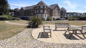 A large building with multiple windows and a paved courtyard with benches. - Solent Landing No 12A - Beachfront (Bembridge)