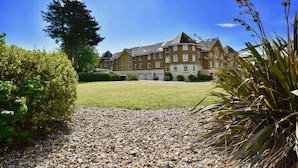 A large, multi-story building with a symmetrical facade, a well-maintained lawn, and a gravel pathway leading to the entrance. - Solent Landing No 12A - Beachfront (Bembridge)