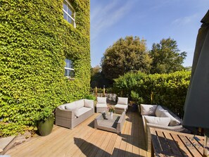 A patio with wicker furniture, a wooden deck, and a building covered in ivy. - Solent Landing No 16 Beach Retreat (Bembridge)