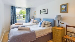 A bedroom with two beds, a wooden dresser, and a lamp. - Solent Landing No 16 Beach Retreat (Bembridge)