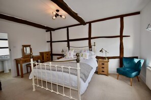 Ein Schlafzimmer mit Himmelbett, Holz-Kopfteil, Nachttischen, einem Frisiertisch und einem blauen Stuhl.