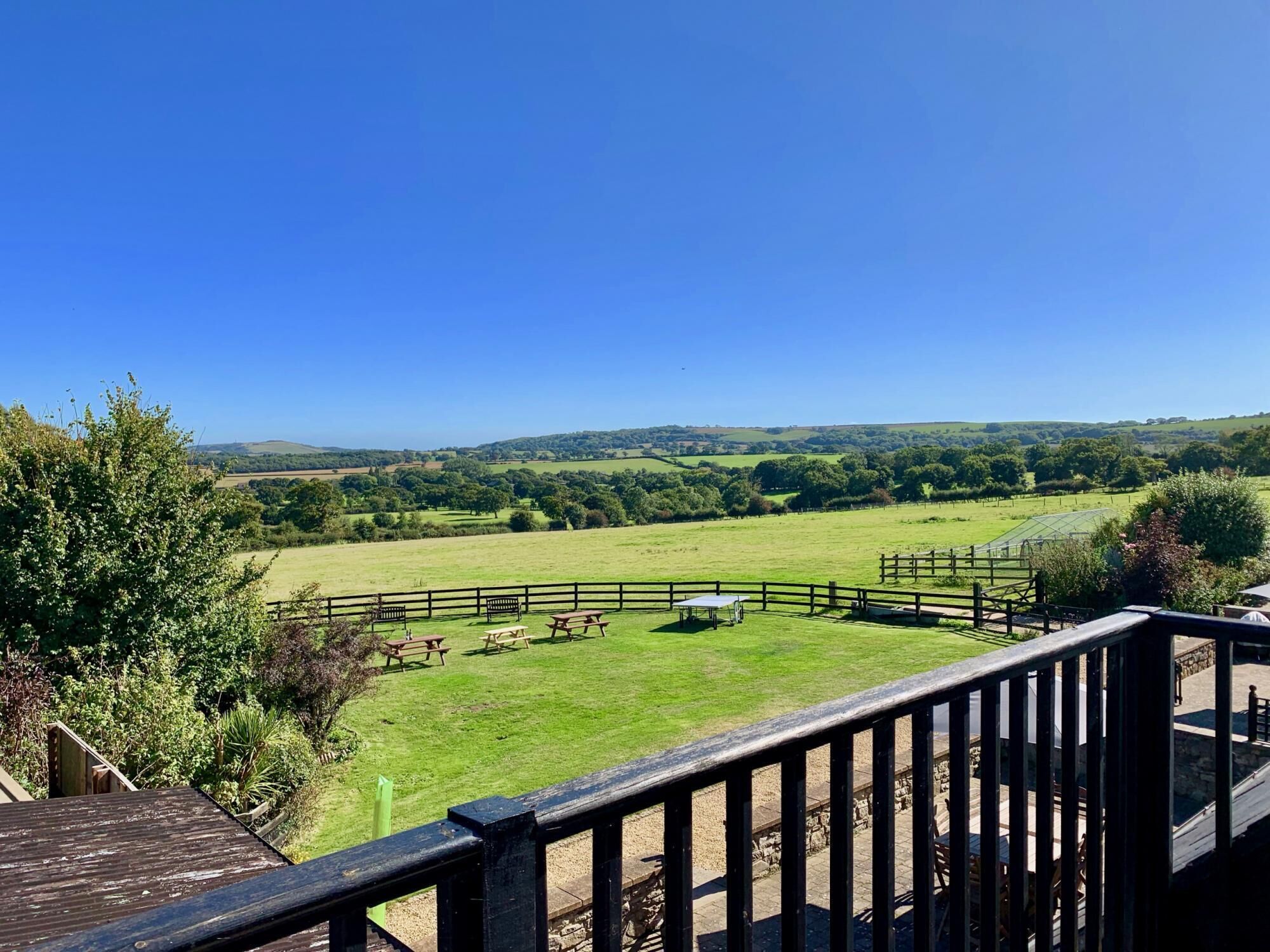 A view from a balcony overlooking a grassy field with picnic tables and a wooden fence.