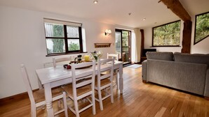 A dining area with a white table and chairs, a gray sofa, wooden flooring, and large windows with a view of greenery. - The Cote Little Upton Farm (Ryde)