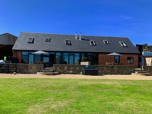 A two-story building with a sloped roof, multiple windows, and a stone wall in front. - Tithe Barn Little Upton Farm (Ryde)
