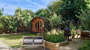 A wooden deck with a bench, a barbecue grill, and a wooden structure with arched windows. - Gothic Cottage Hot Tub Fire Pit Pizza Oven Gas Bbq (Ryde)