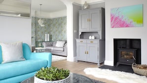 A living room with a blue sofa, grey cabinets, a fireplace, and a wall with a floral wallpaper. - Gothic Cottage Hot Tub Fire Pit Pizza Oven Gas Bbq (Ryde)