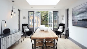 A modern dining area with a high ceiling and skylight, featuring a wooden table and black chairs. - Gothic Cottage Hot Tub Fire Pit Pizza Oven Gas Bbq (Ryde)