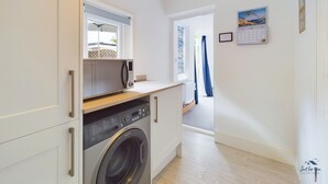 A compact kitchen with a washing machine, a microwave, and a calendar on the wall. - Coastal East View in St Helens (Ryde)