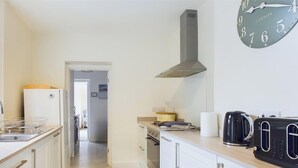 A kitchen with a sink, stove, toaster, and a clock on the wall. - Coastal East View in St Helens (Ryde)