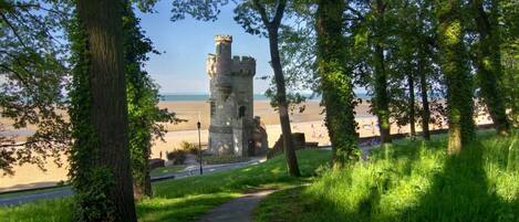 A pathway leading to a stone tower with a view of a beach and ocean.