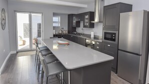 A modern kitchen with a central island, stainless steel appliances, and a sliding glass door leading to a balcony. - Seaside Cottage in Ryde (Ryde)