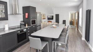 A modern kitchen with a central island, built-in appliances, and a dining area with bar stools. - Seaside Cottage in Ryde (Ryde)