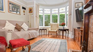 Un salon chaleureux avec une grande baie vitrée, un canapé confortable, un pouf rouge, un meuble en bois et un téléviseur.