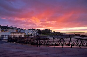 Une promenade en bord de mer avec une rambarde en métal, des bâtiments en arrière-plan et un ciel au coucher du soleil.