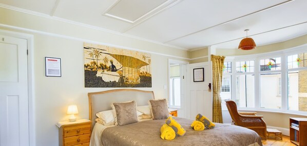 A bedroom with a bed, a nightstand, a chair, a window, and a painting on the wall. - Anchor Down Close to the Beach Cafes and Restaurants (Ryde)