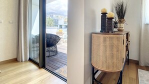 Uma sala de estar moderna com uma porta de vidro deslizante que dá para uma varanda, uma mesinha de vime com objetos decorativos e uma cadeira trançada preta.