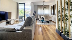 Uma sala de estar moderna com sofá, TV e área de jantar com cadeiras e mesa.