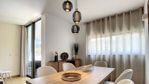 Uma sala de jantar moderna com uma mesa de madeira, cadeiras brancas e iluminação pendente.